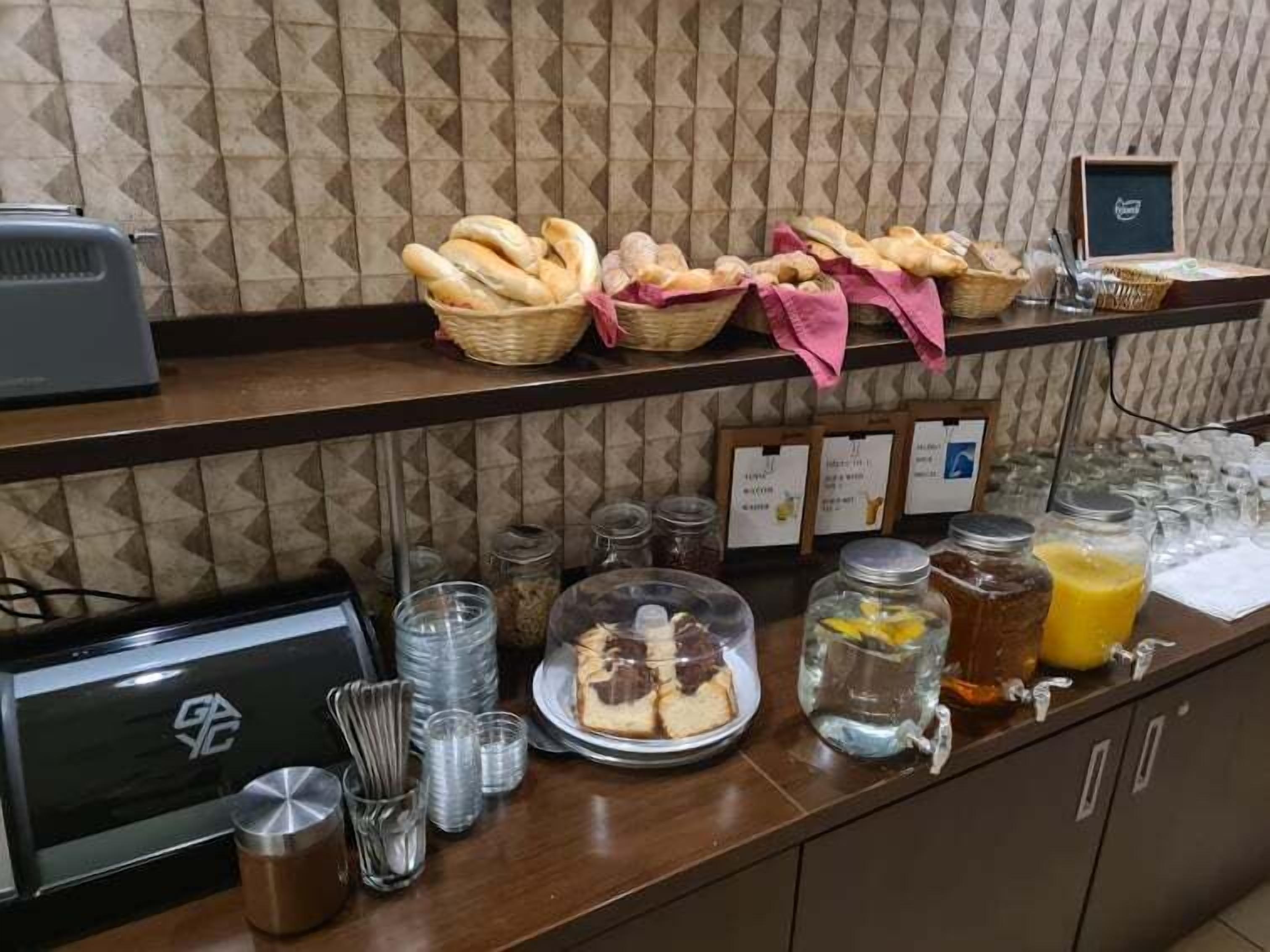 A buffet area with bread, pastries, and a juice dispenser.