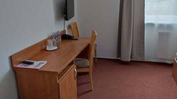 Habitació amb escriptori de fusta, cadira, televisió penjada a la paret i finestra amb cortines.
