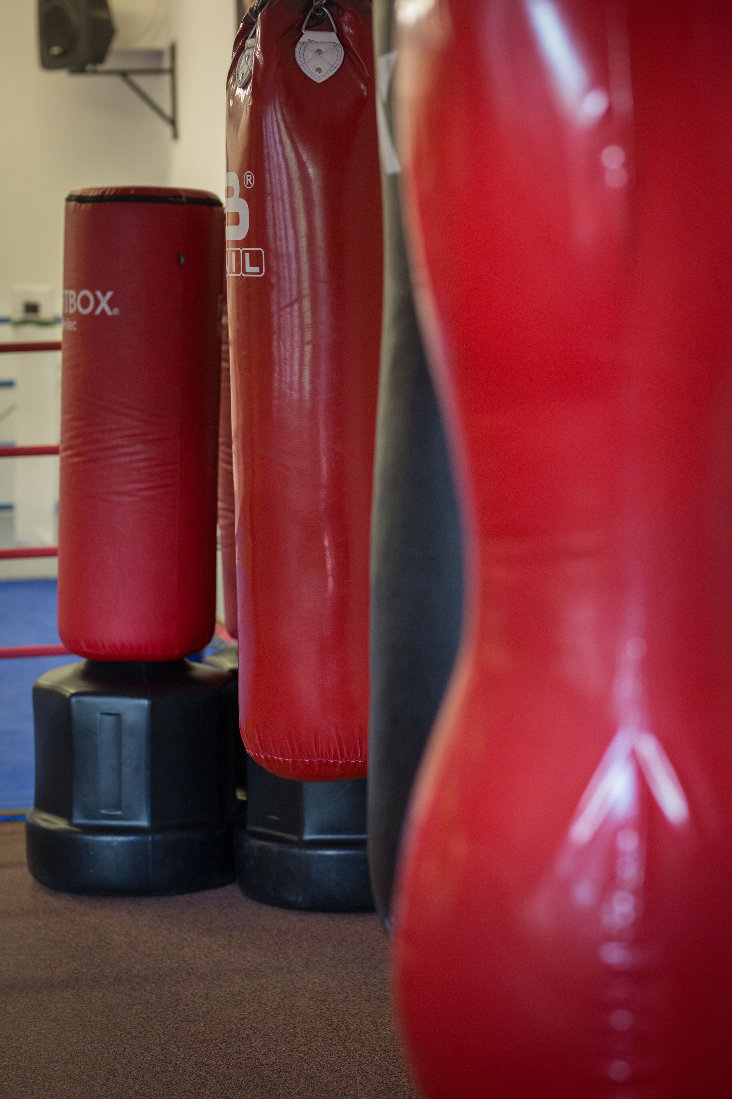 Tres sacos de boxeo rojos de distintos tamaños sobre bases negras en un gimnasio.