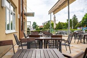 Un espacio al aire libre con mesas y sillas, un edificio con una ventana y un cartel.