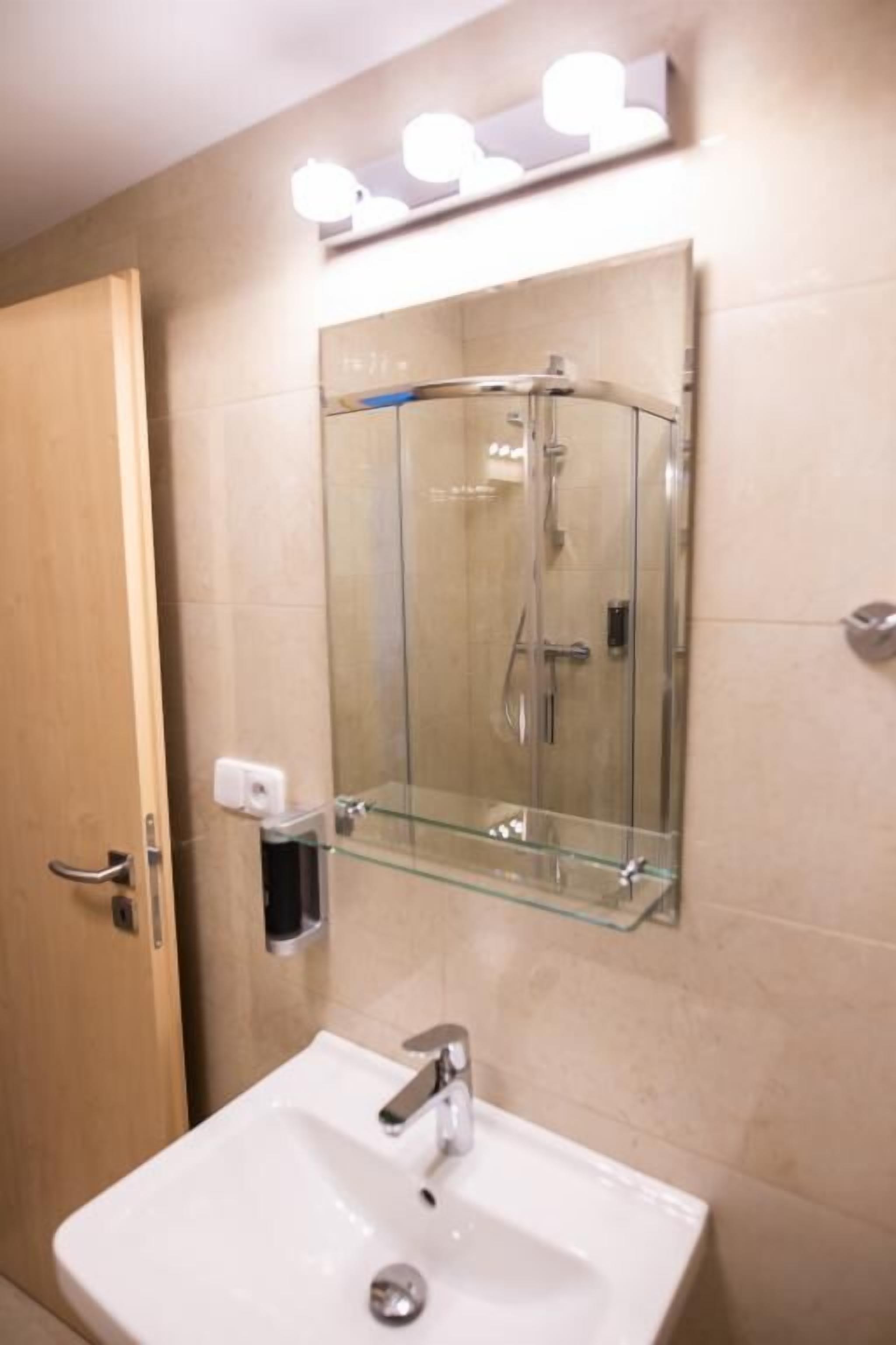 A bathroom with a glass shower enclosure, a white sink, and a mirror with lights above it.