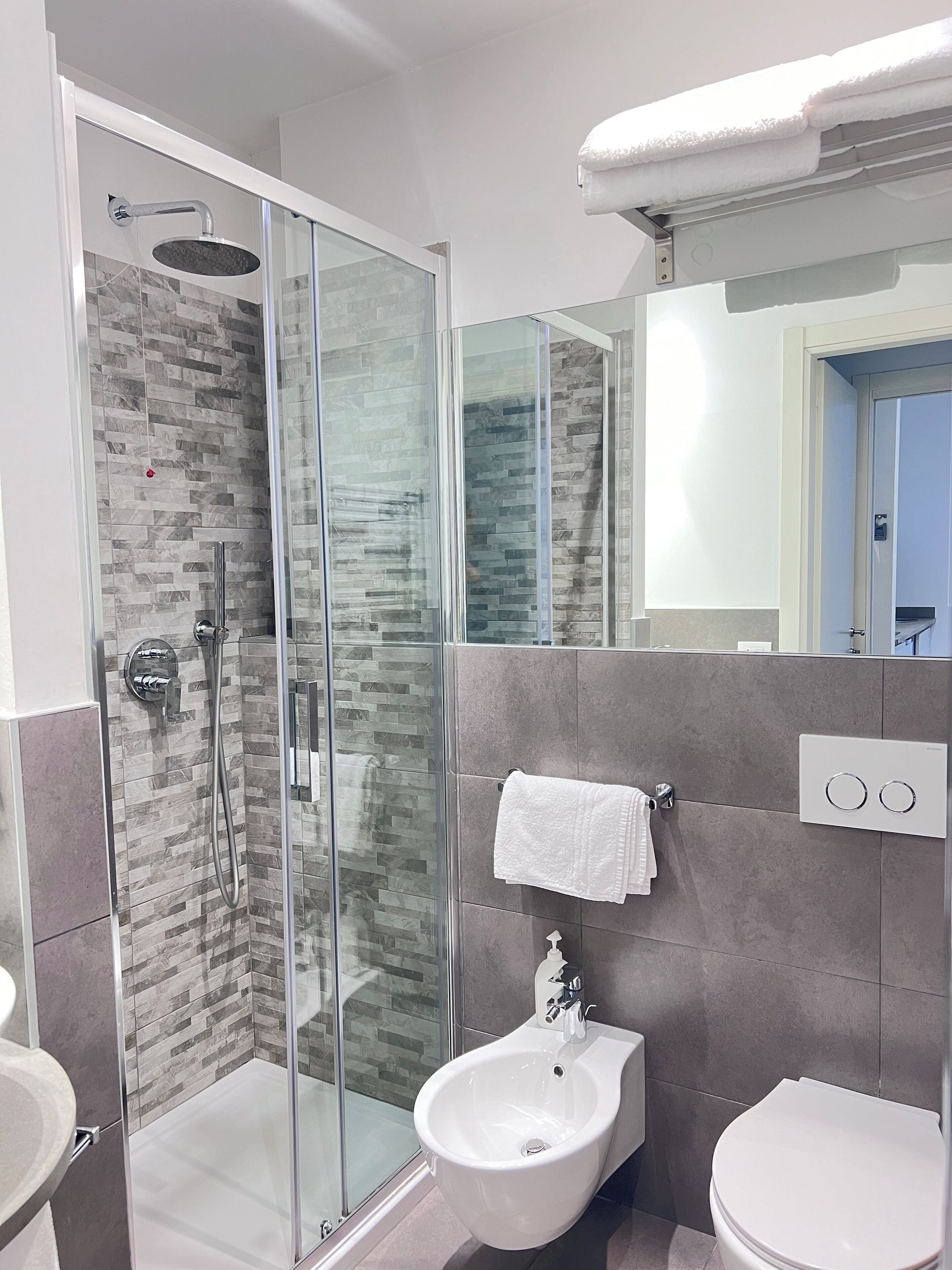 Een moderne badkamer met een glazen douchecabine, een wastafel op een voetstuk en een toilet.