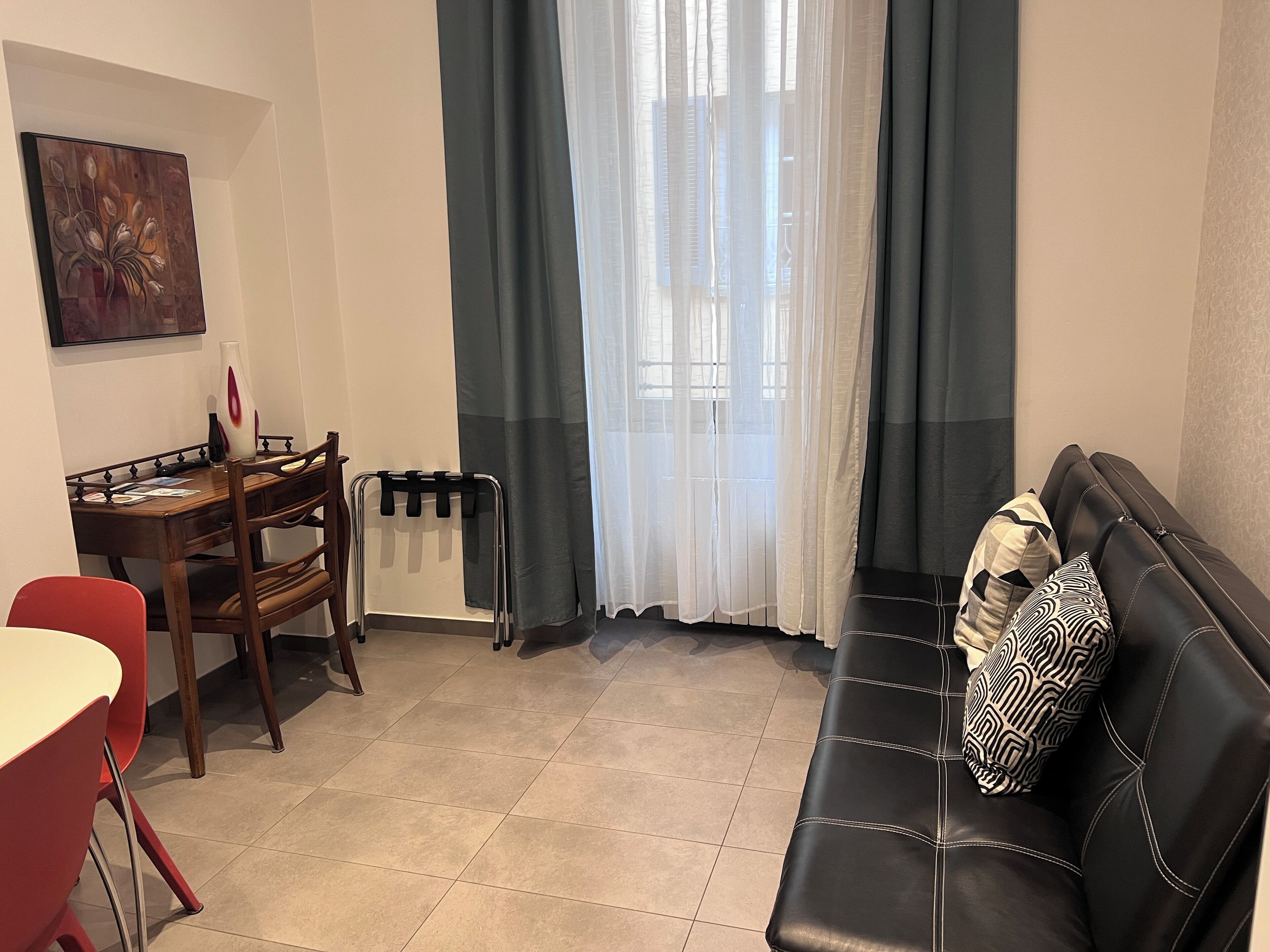 Ein Wohnzimmer mit schwarzem Ledersofa, einem Holzesstisch mit Stühlen, einer Heizung und einem Bild an der Wand.