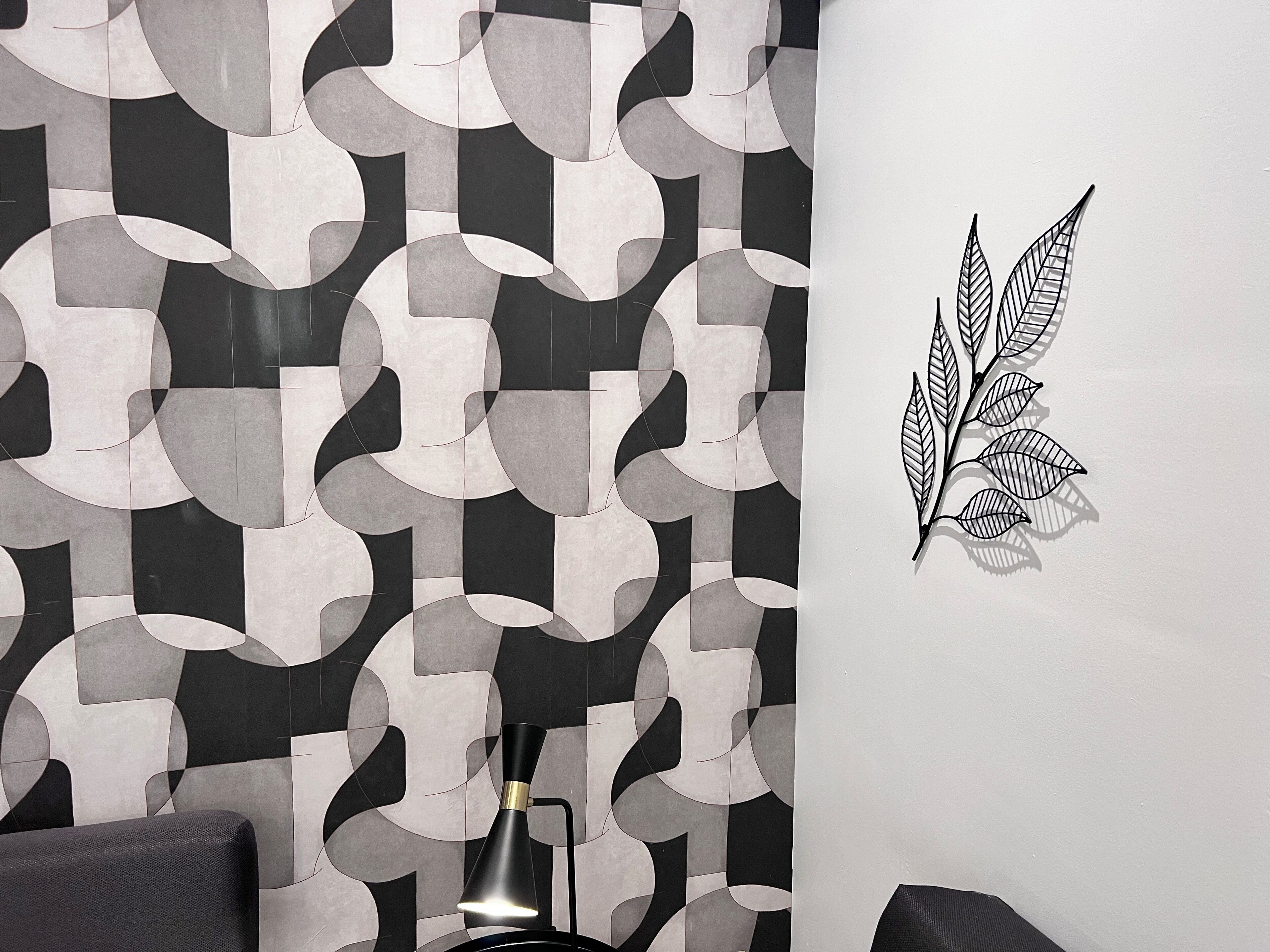 Una stanza con una parete a motivo geometrico, una lampada da terra nera e una decorazione a forma di foglia fissata al muro.