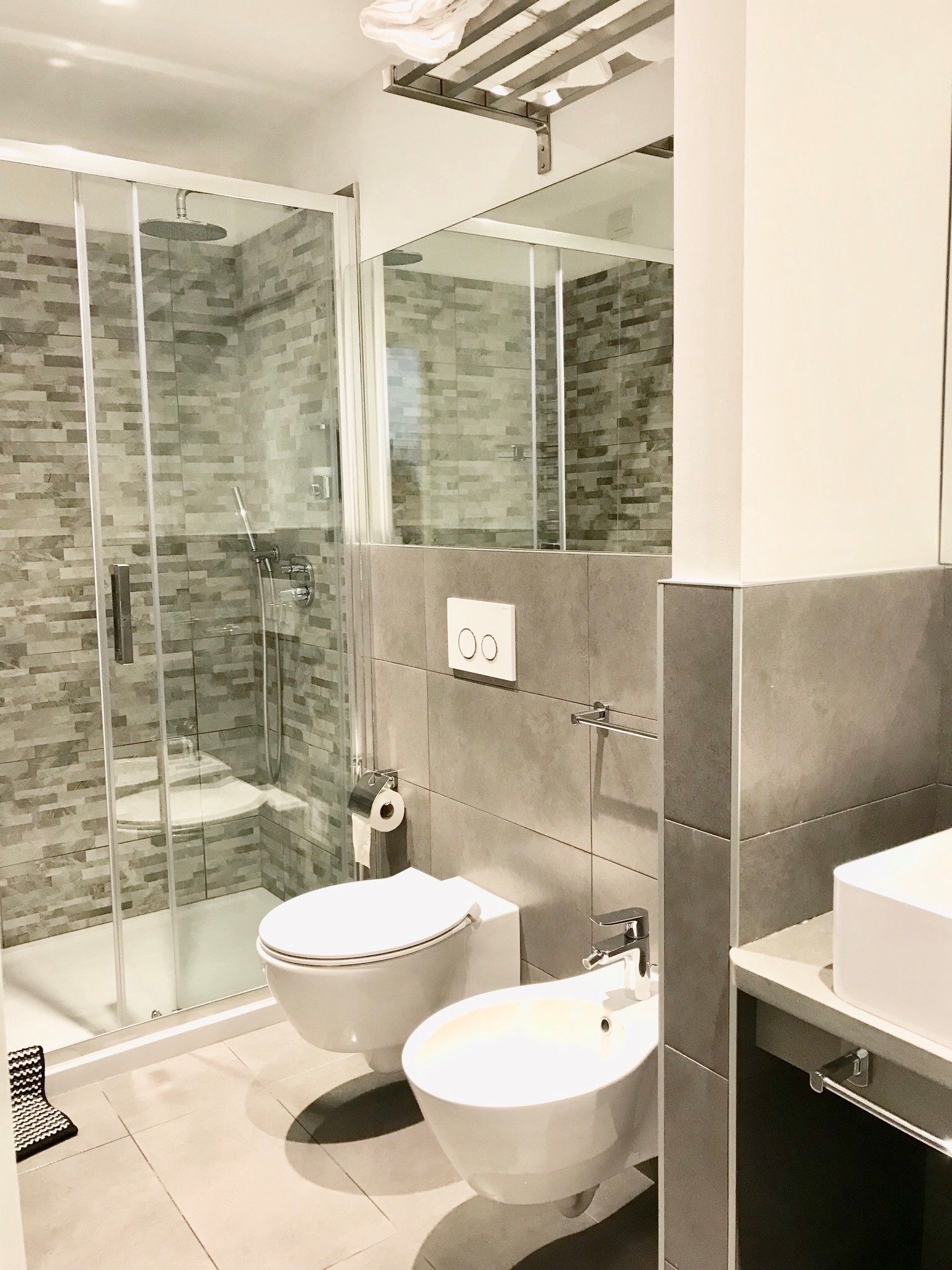 A modern bathroom with a glass-enclosed shower, two toilets, a bidet, and a large mirror.