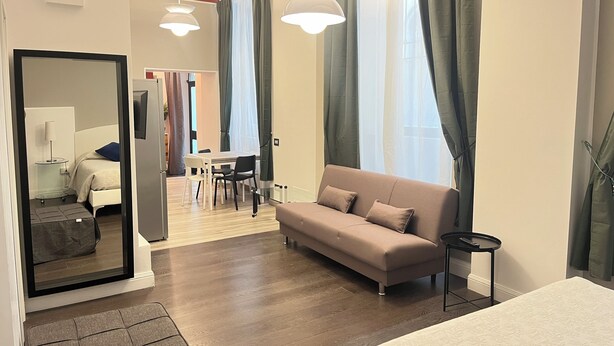 A modern hotel room with a sofa, a dining table with chairs, a mirror, and a TV. - Residence Diaz (Como)