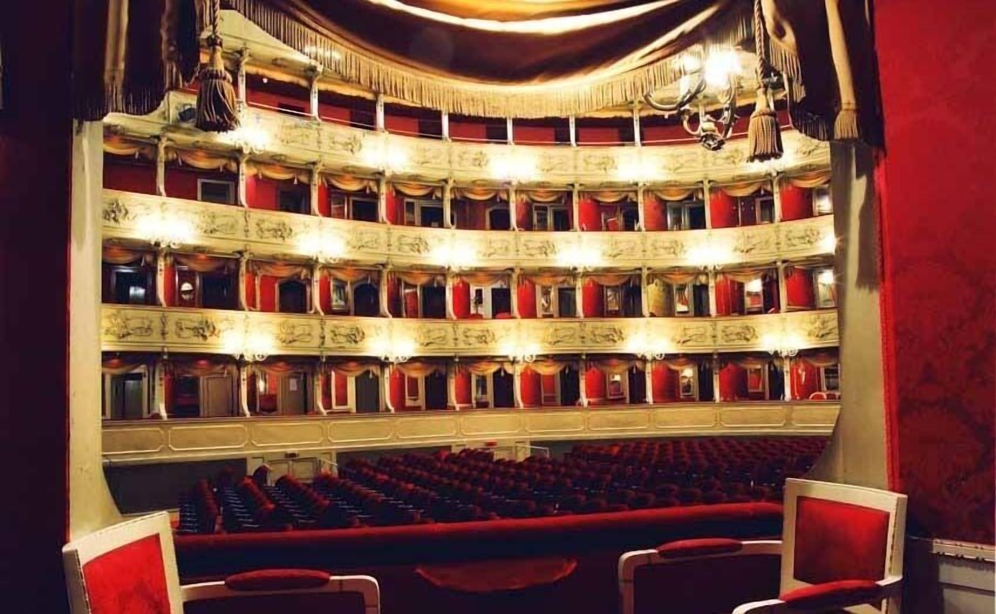 Un teatro de varios niveles con hileras de asientos rojos y detalles arquitectónicos ornamentales.