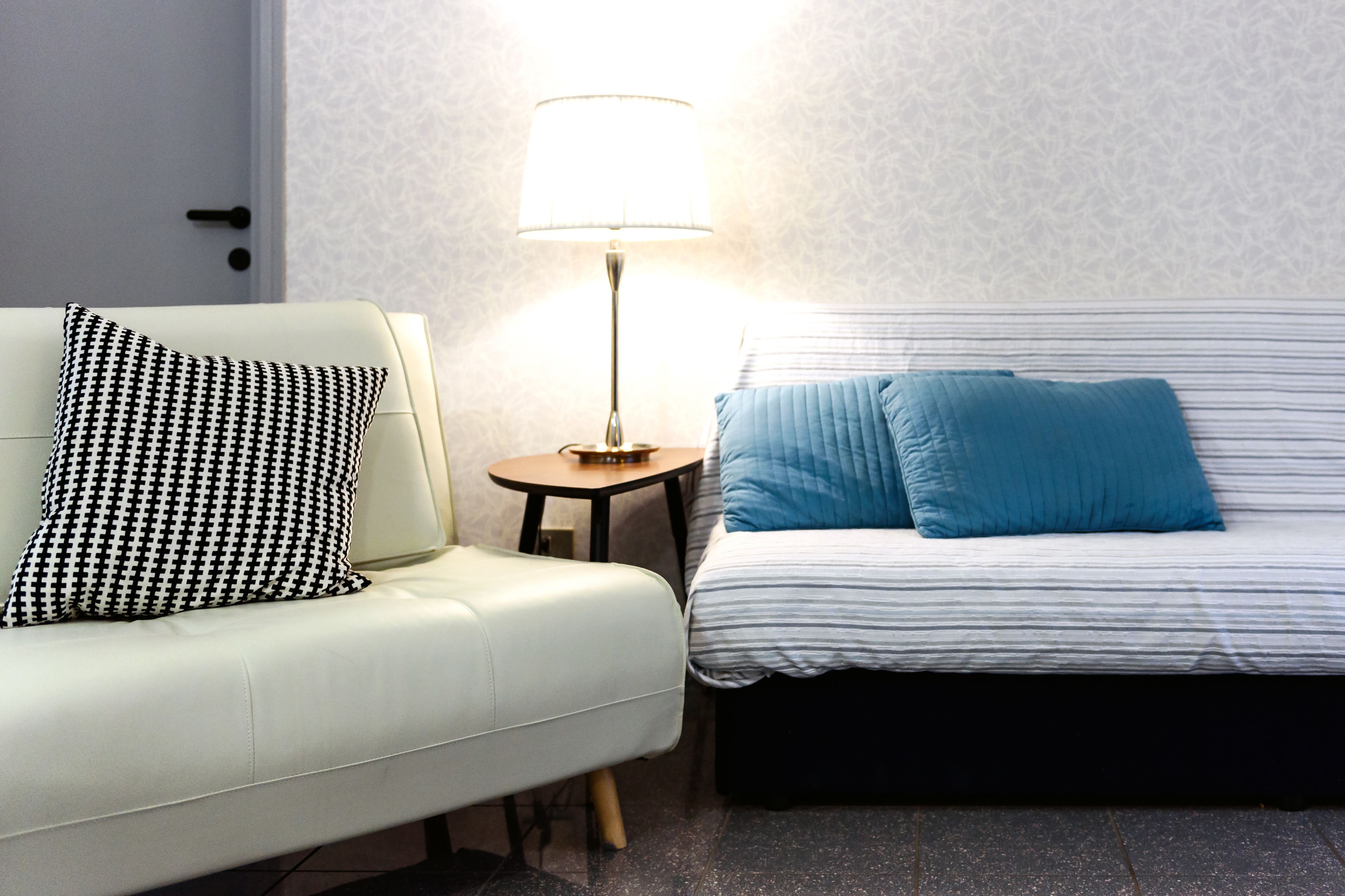 Habitación de hotel con un sofá blanco, una mesita redonda con una lámpara y una cama con ropa de cama a rayas.