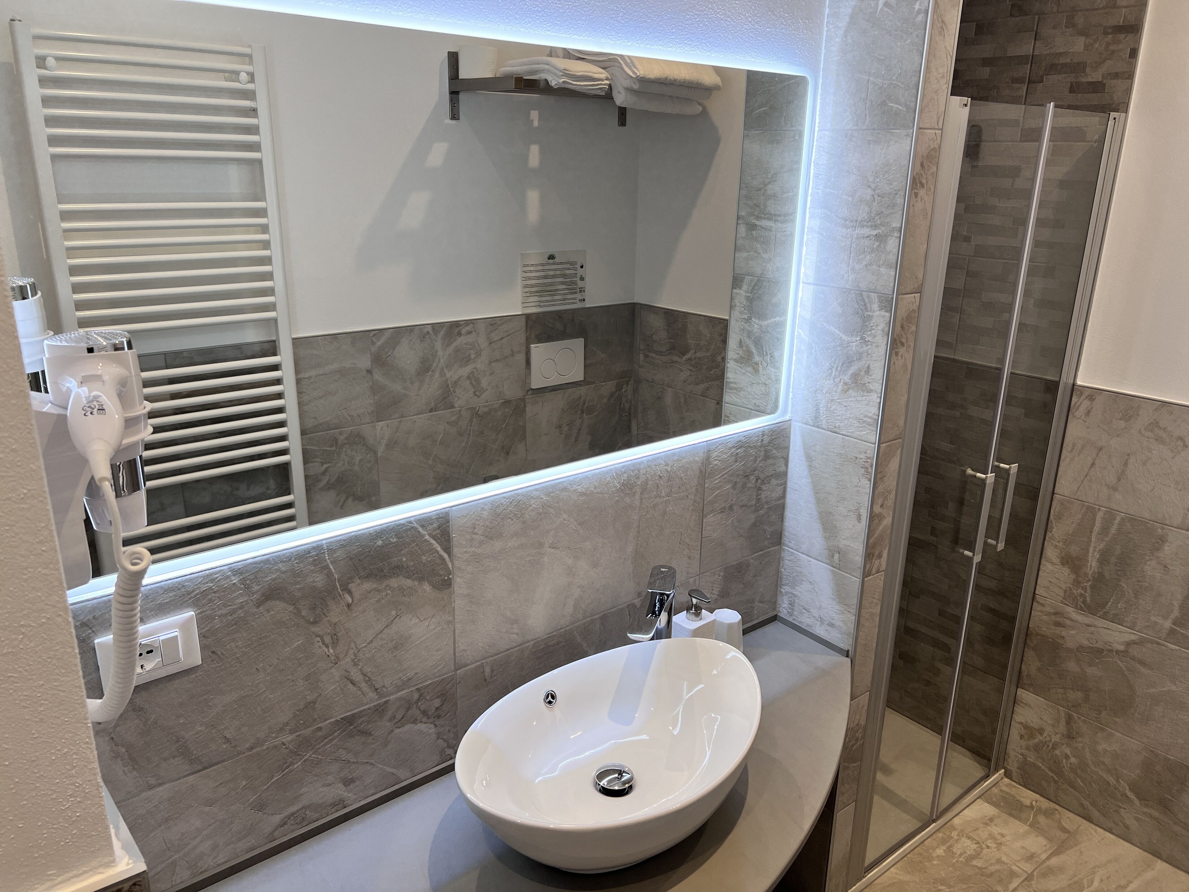 Un baño moderno con un espejo grande, un lavabo integrado y una cabina de ducha de vidrio.