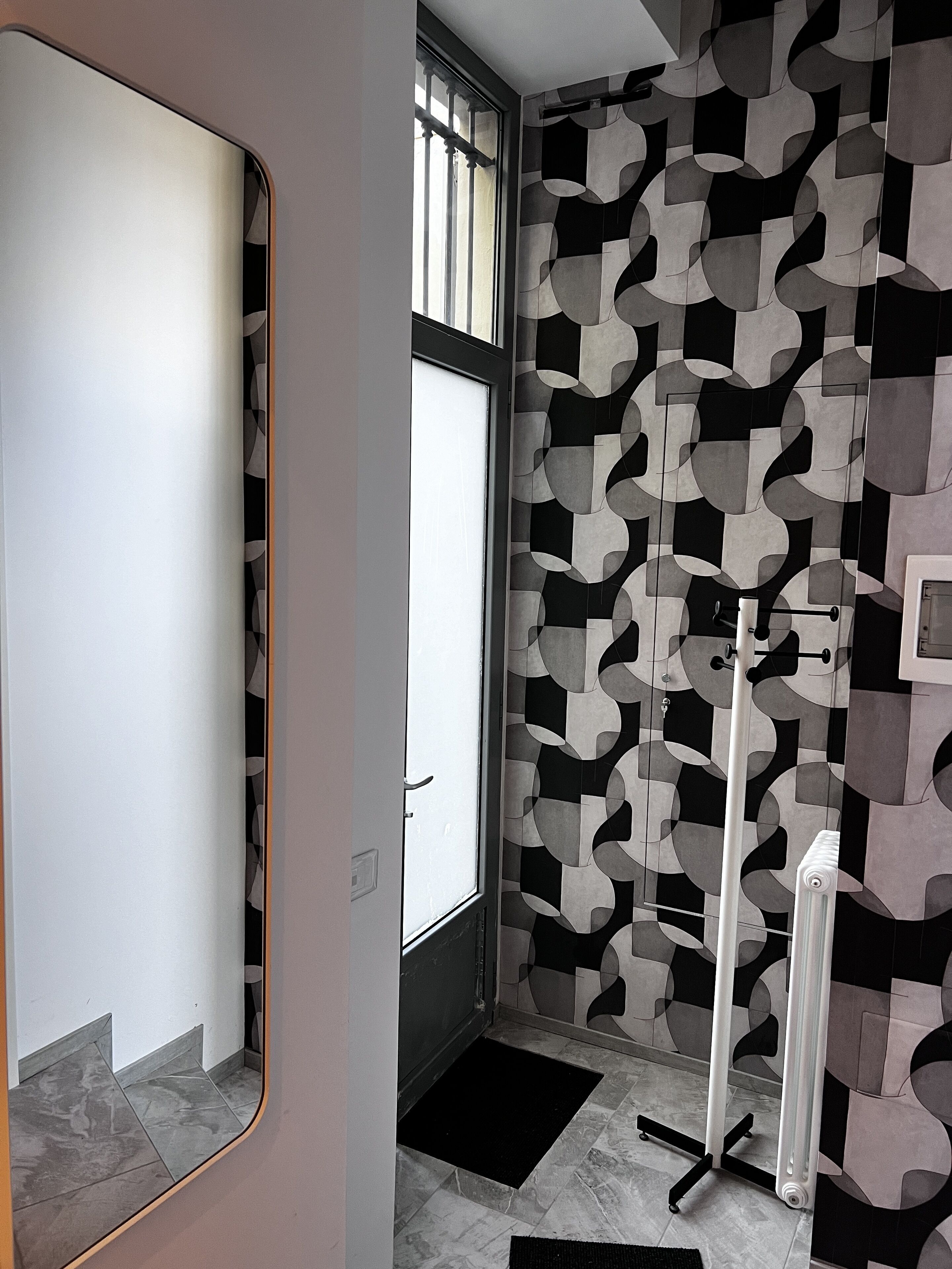 Ein modernes Badezimmer mit Wand in geometrischem Muster, einem großen Spiegel und einer Heizung.