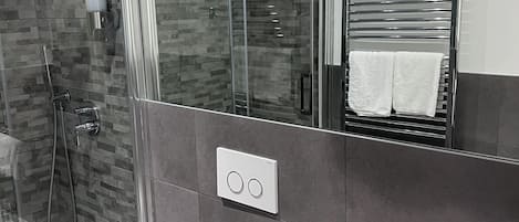 Un baño moderno con cabina de ducha de vidrio, inodoro blanco, toallero y espejo.