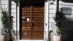 A wooden double door with a mail slot and a doorbell. There is a potted plant with flowers to the right of the door. - Residence Diaz (Como)