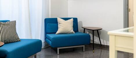 A small, modern room with a blue sofa, a small table, and a white wall with a shelf.