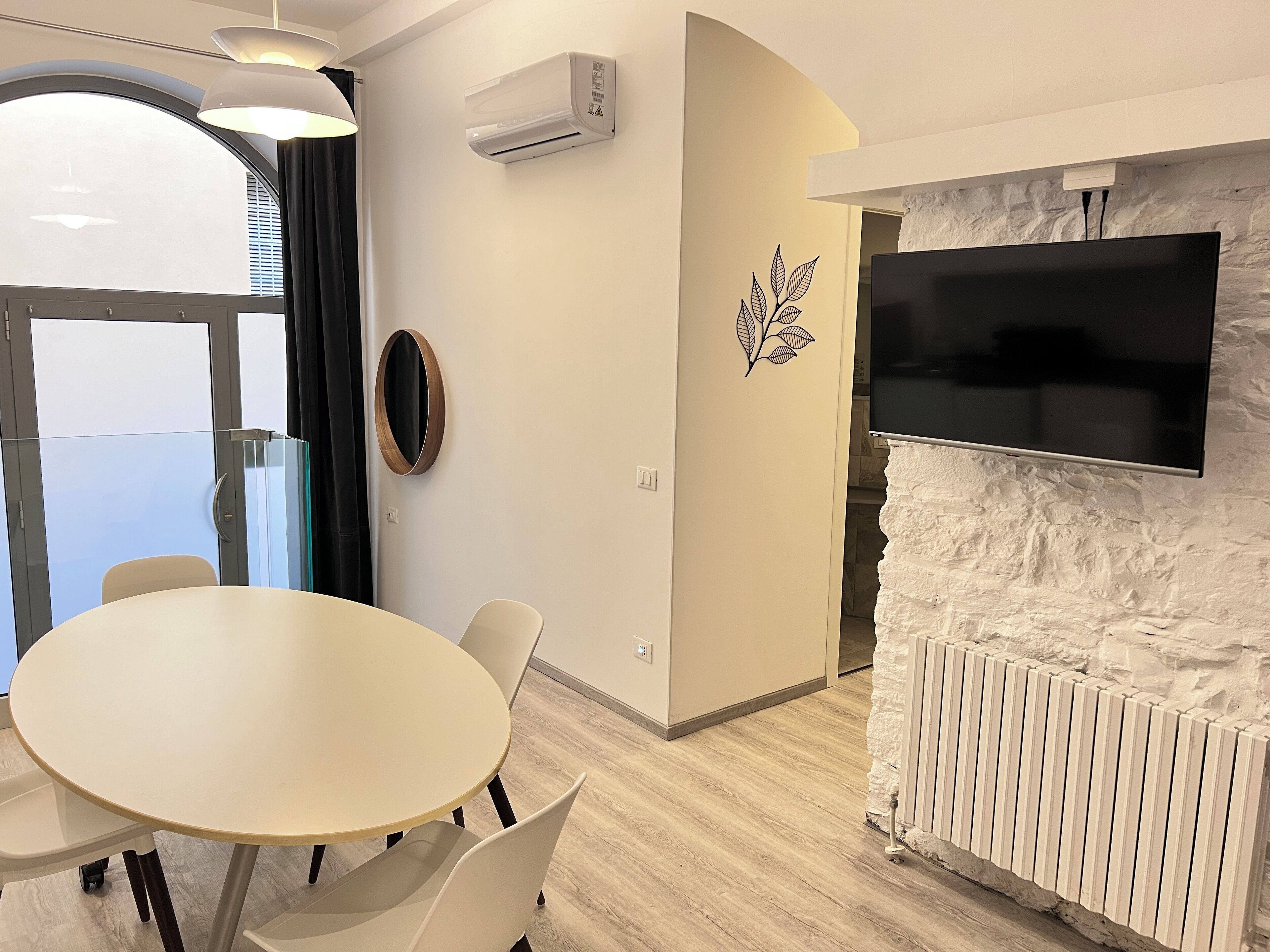 A modern room with a round table, chairs, a mounted TV, an air conditioner, and a decorative leaf wall decal.