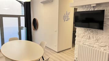 A modern room with a round table, chairs, a mounted TV, an air conditioner, and a decorative leaf wall decal.
