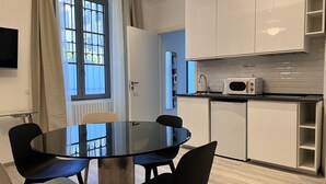 A modern kitchen with white cabinets, a microwave, and a sink. There is a round glass table with four chairs. - Residence Diaz (Como)