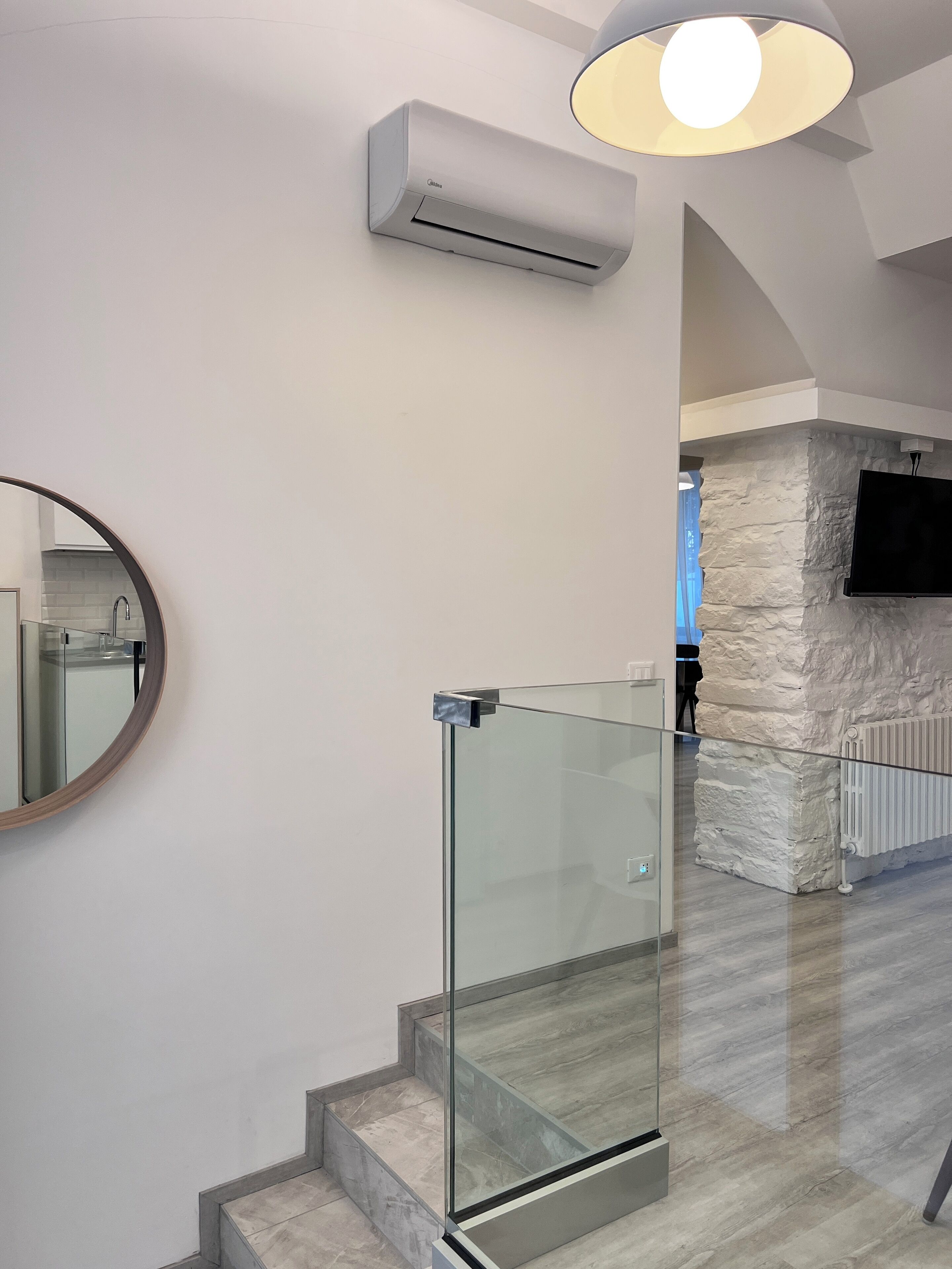 Um interior moderno com escada em guarda-corpo de vidro, ar condicionado fixado na parede e um detalhe de parede em pedra.