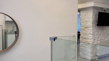 Un interno moderno con scala dotata di ringhiera in vetro, condizionatore a muro e parete decorativa in pietra.