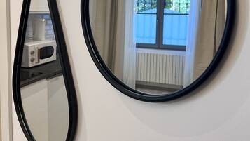Une pièce avec un mur blanc, un miroir noir et une fenêtre avec des rideaux.
