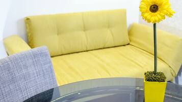 A yellow sofa, a gray pillow, and a yellow vase with a sunflower.