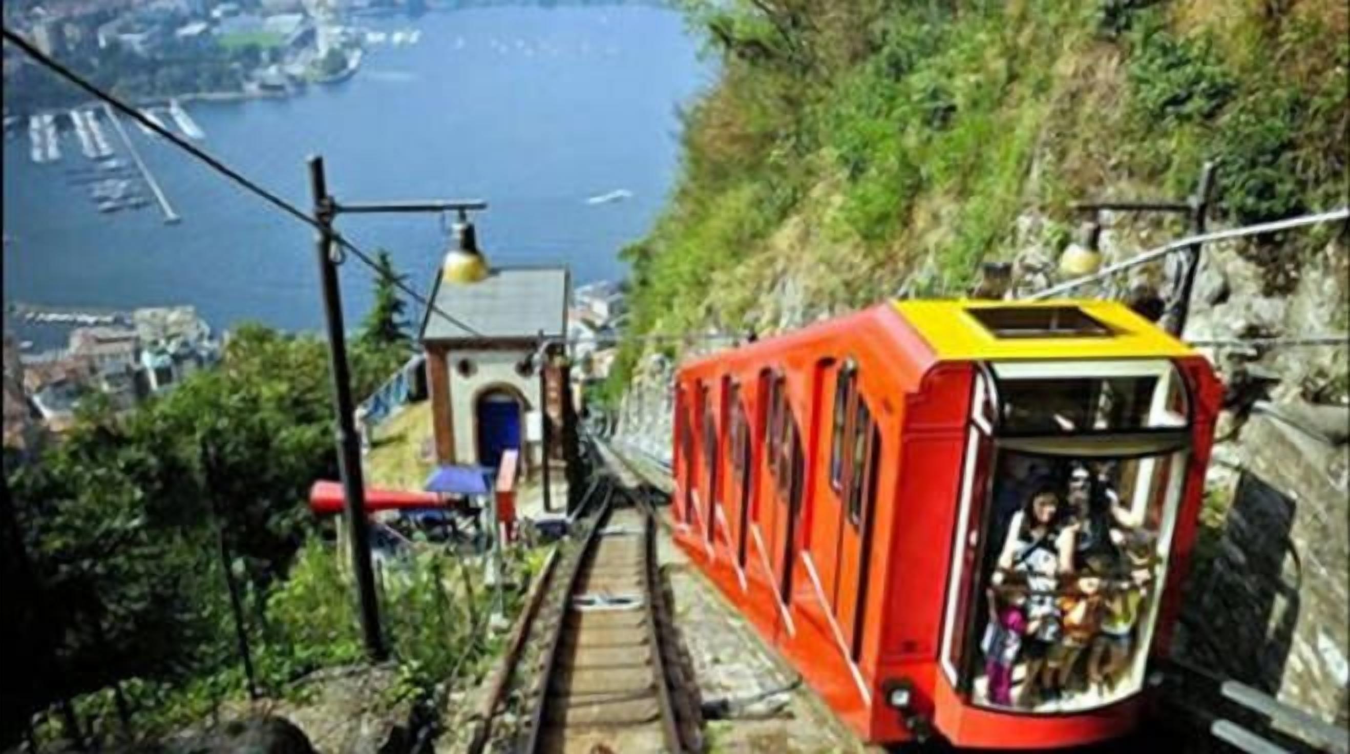 Un teleférico asciende por una pendiente pronunciada, con vistas a una masa de agua y edificios al fondo.