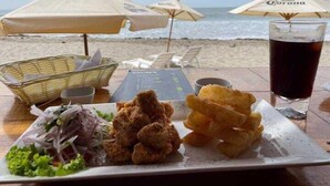 A beachside dining table with a plate of fried food, a glass of dark beverage, and a menu. - Don Giovanni Máncora (Máncora)