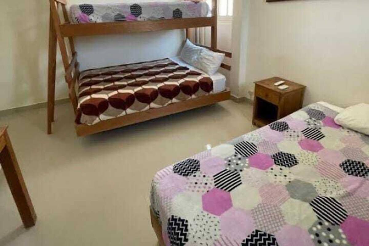 A room with a bunk bed, a single bed, a small table, and a painting on the wall.