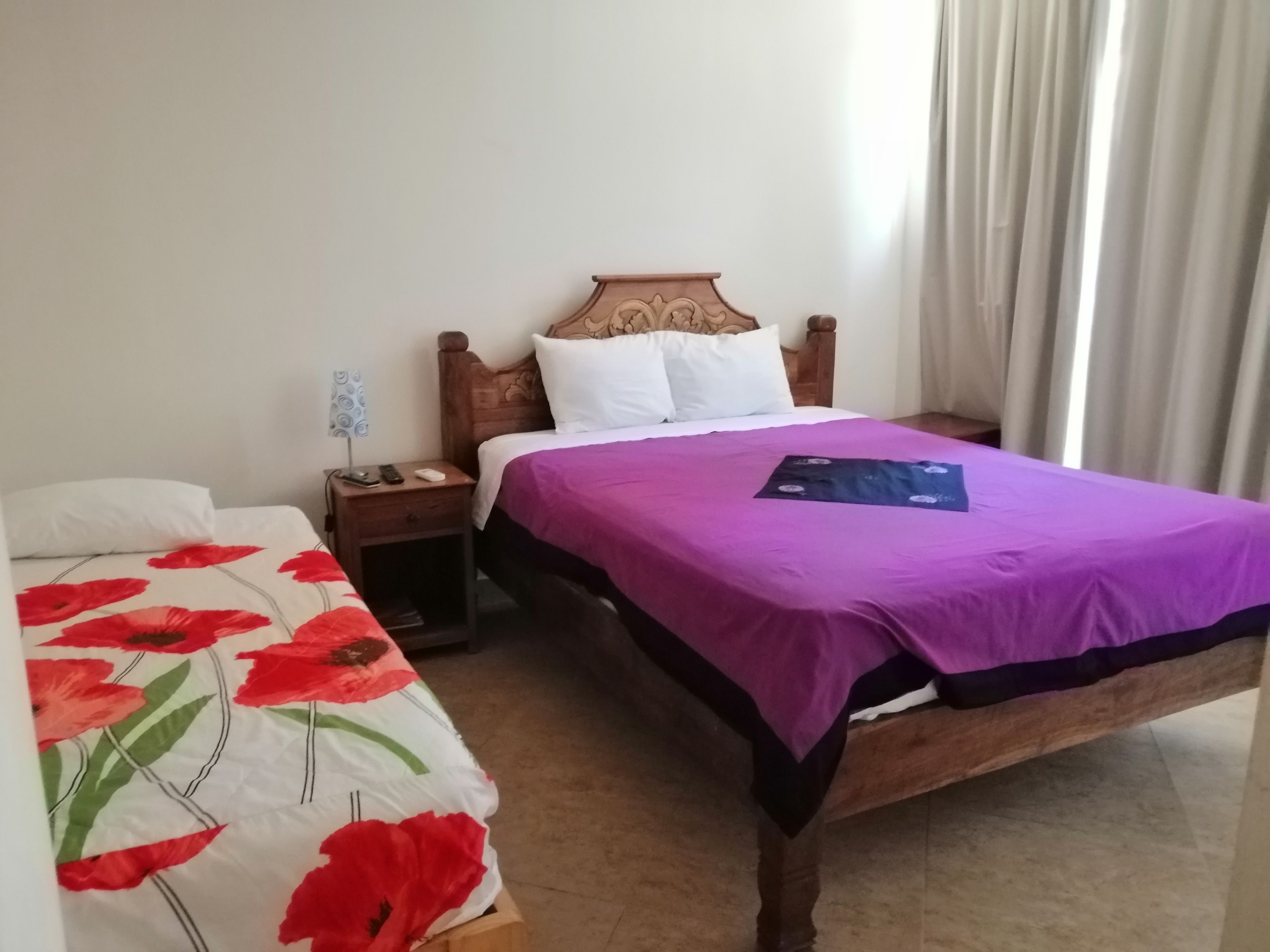 Habitación de hotel con una cama de madera, una mesita de noche y una ventana con cortinas.