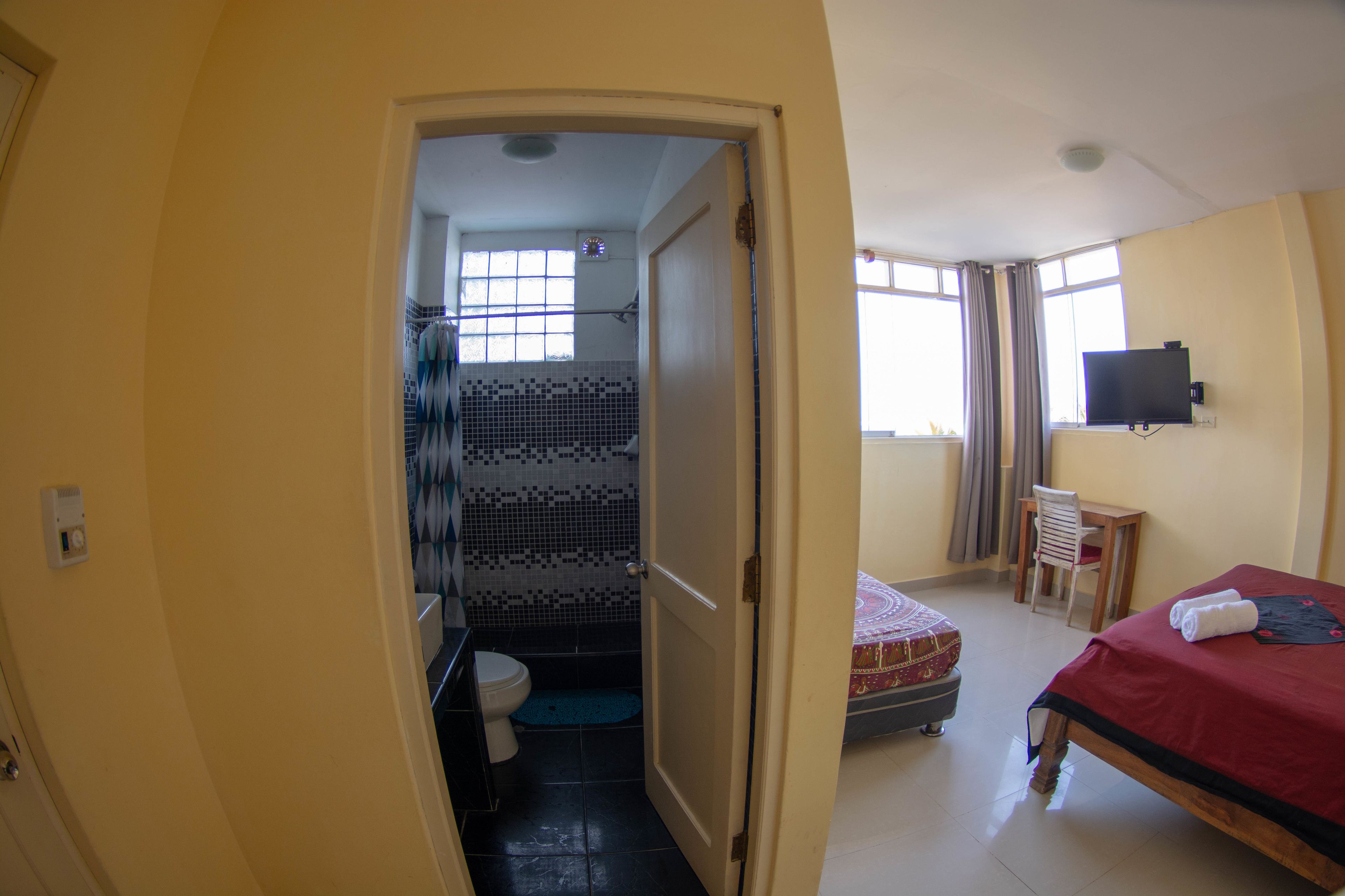 Una habitación con cama, escritorio, silla, televisión y baño completo.