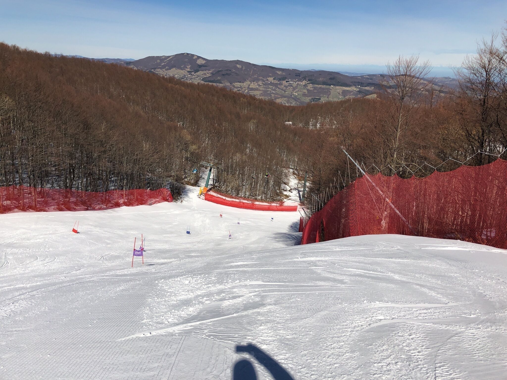 Pista da sci con rete di sicurezza rossa, cielo sereno e montagne sullo sfondo.