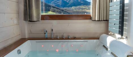 Un baño moderno con detalles de madera, una bañera con múltiples jets y vistas a montañas a través de una ventana.