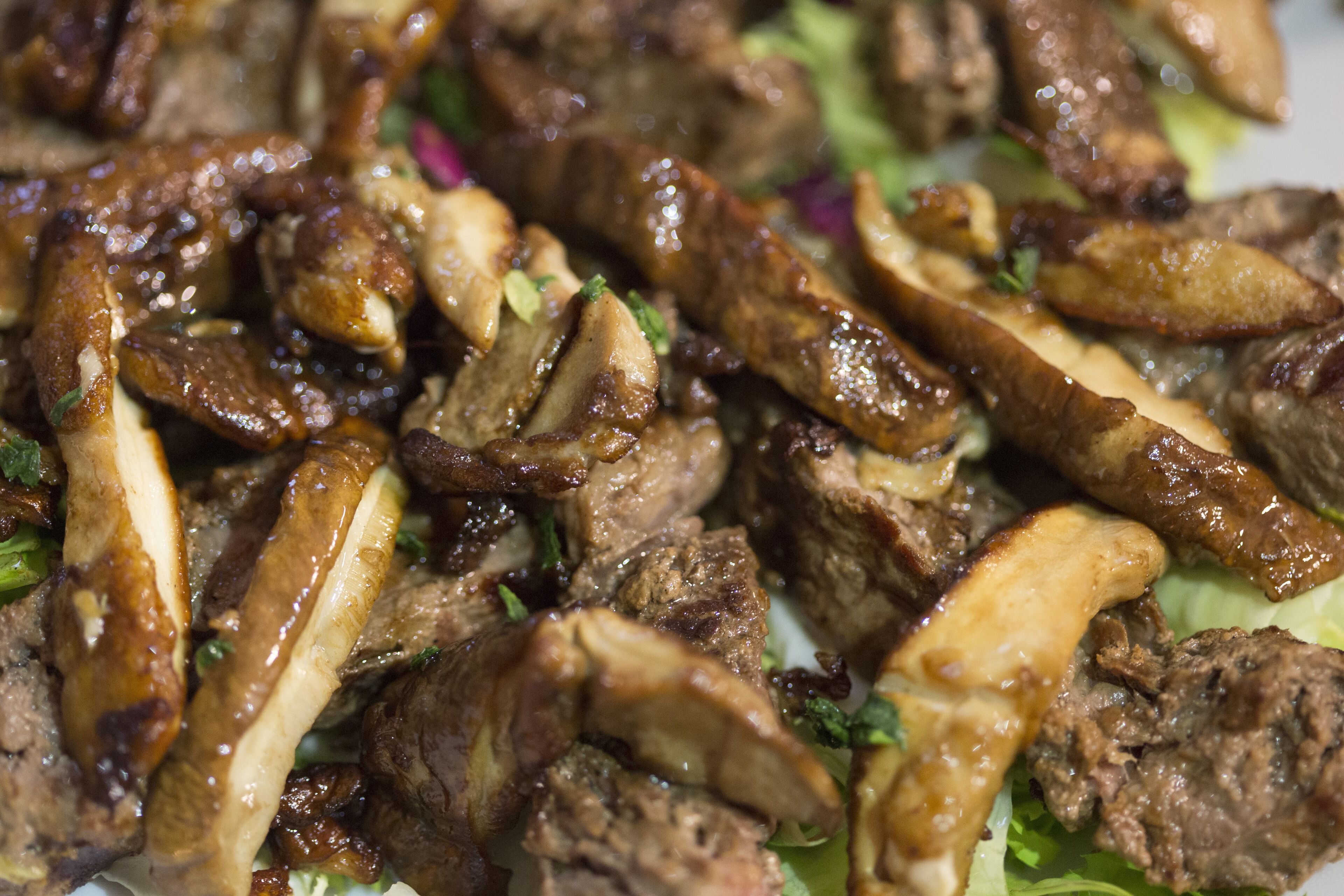 Un primo piano di un piatto con carne a fette e funghi, guarnito con erbe aromatiche.