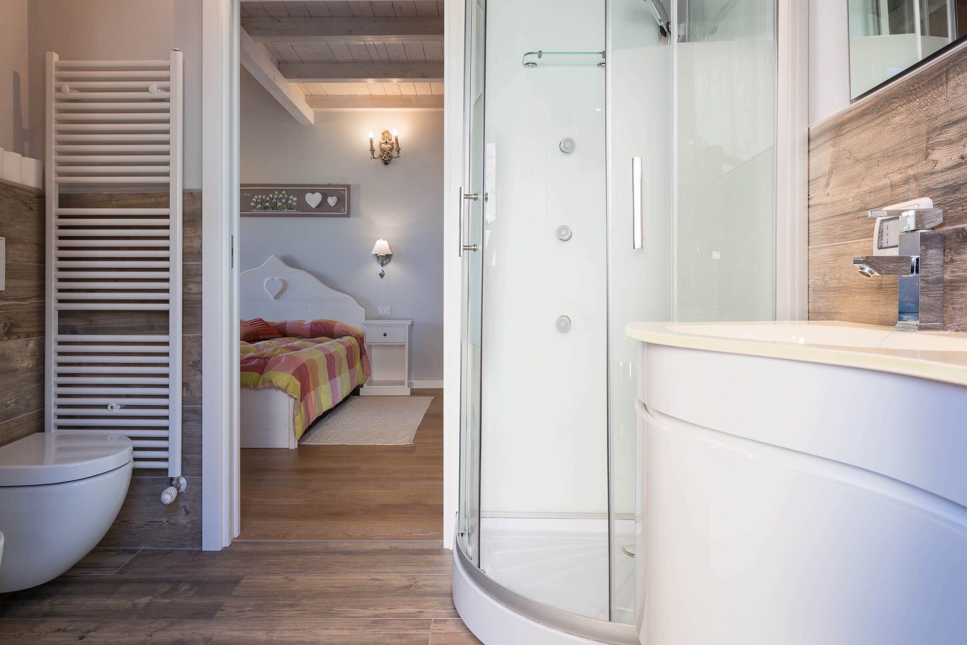 A modern bathroom with a glass shower enclosure, a white toilet, and a wooden floor.