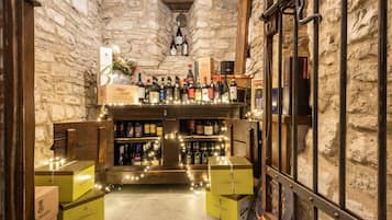 Un estrecho pasillo de paredes de piedra con una zona de bar de madera, que muestra varias botellas y cajas, probablemente de vino o licores.