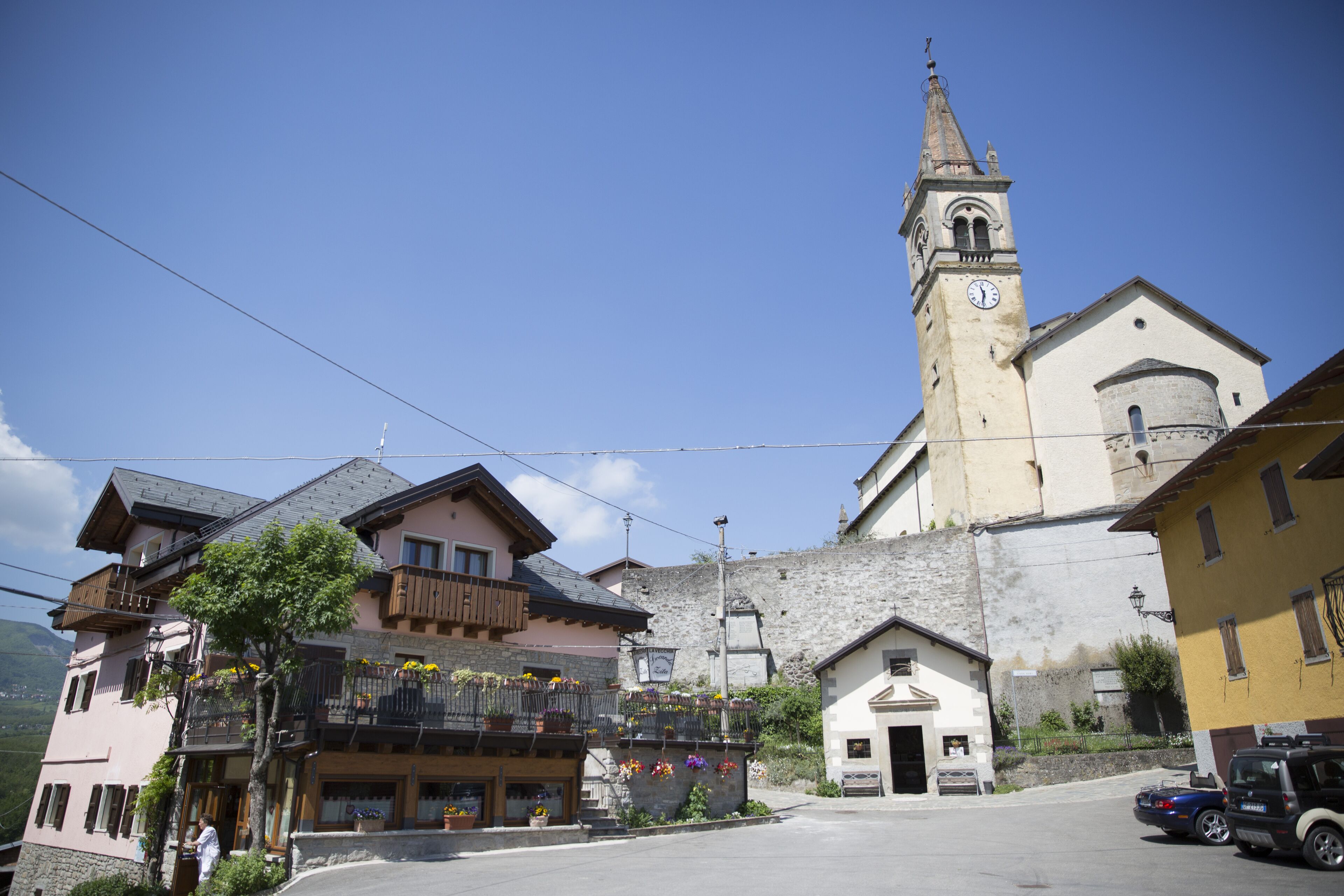 A town square with a church, a building with balconies, and a parked car.