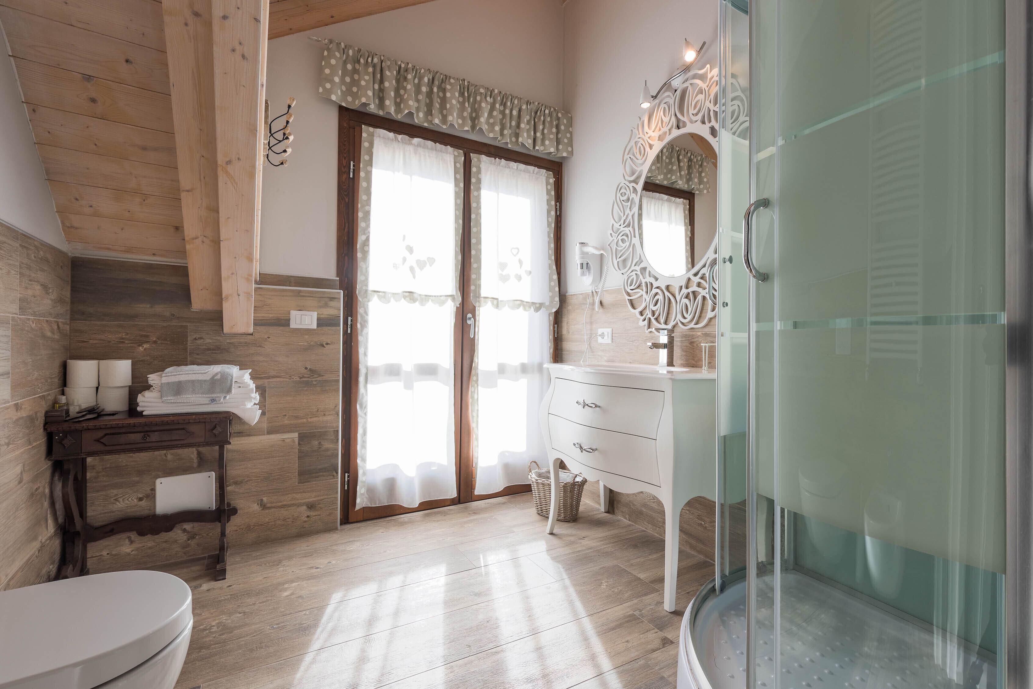 A bathroom with a wooden ceiling, a white sink, a glass shower enclosure, and a large mirror with ornate detailing.