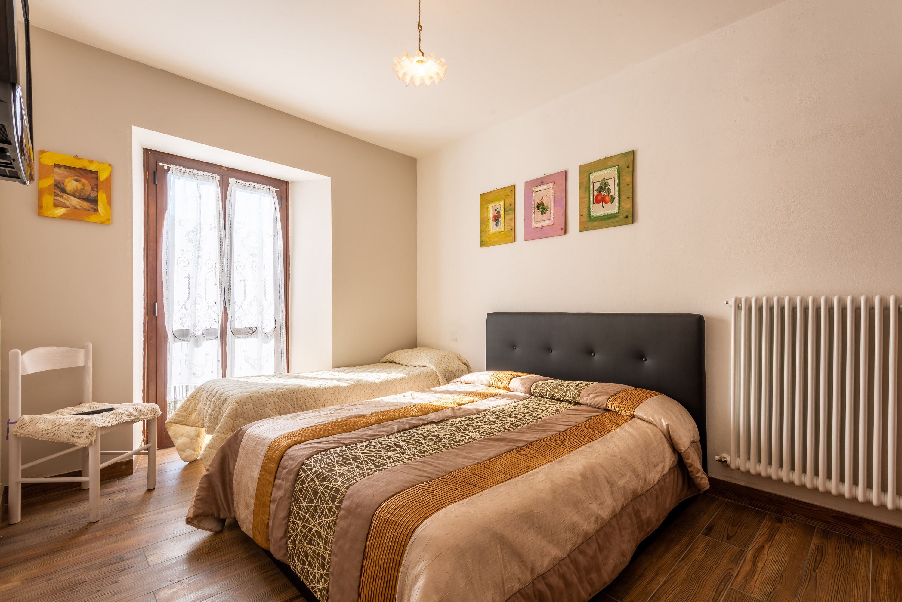 Une chambre avec deux lits, une chaise, un radiateur et trois tableaux encadrés accrochés au mur.