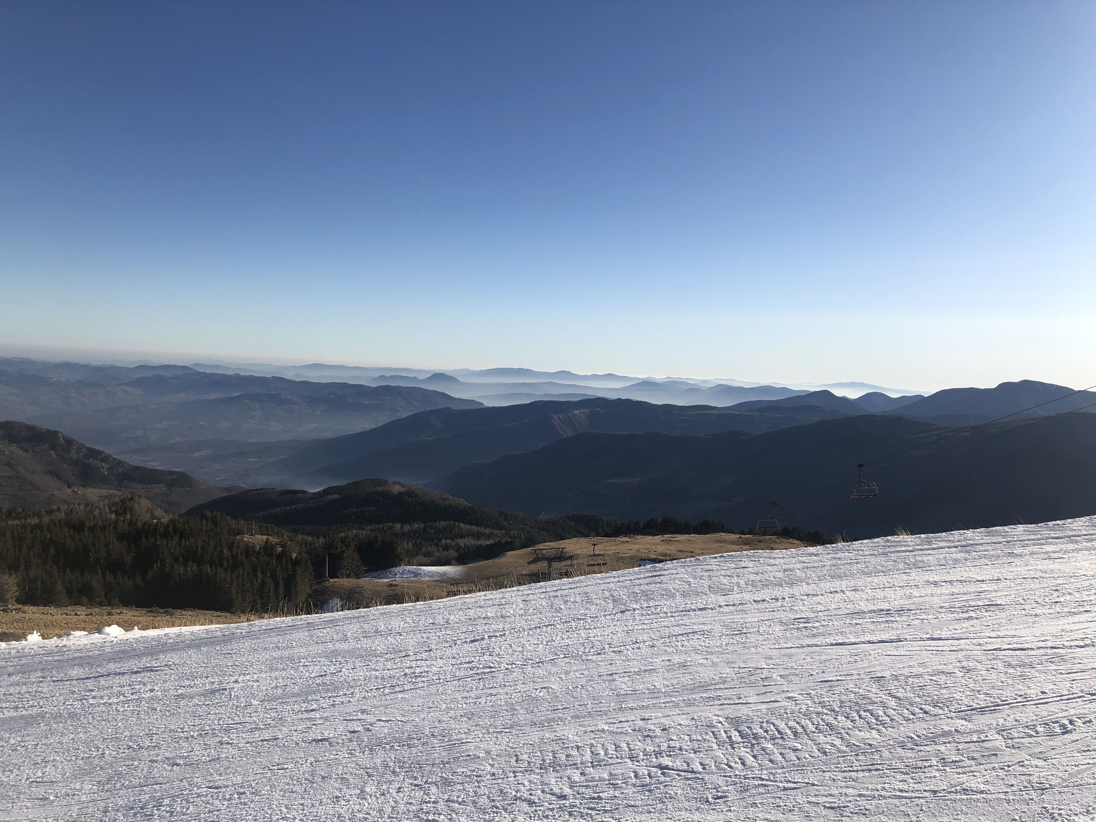 Ein verschneiter Berghang mit einer Seilbahn und fernen Bergketten.