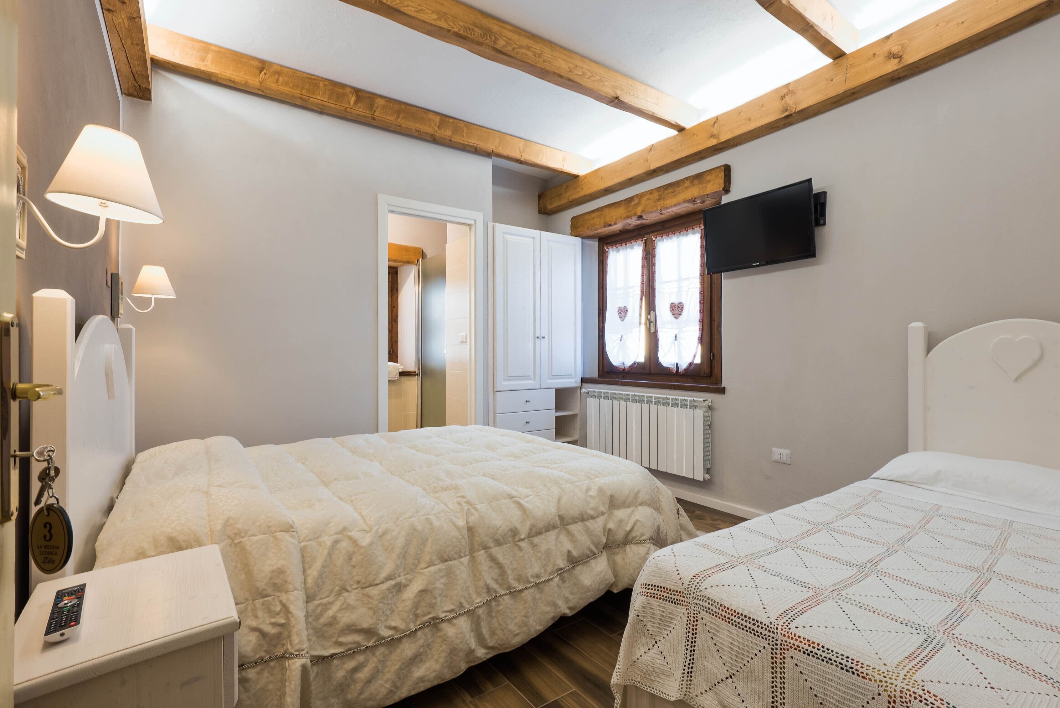 Une chambre avec deux lits, une télévision et une salle de bain comprenant des toilettes et un lavabo.
