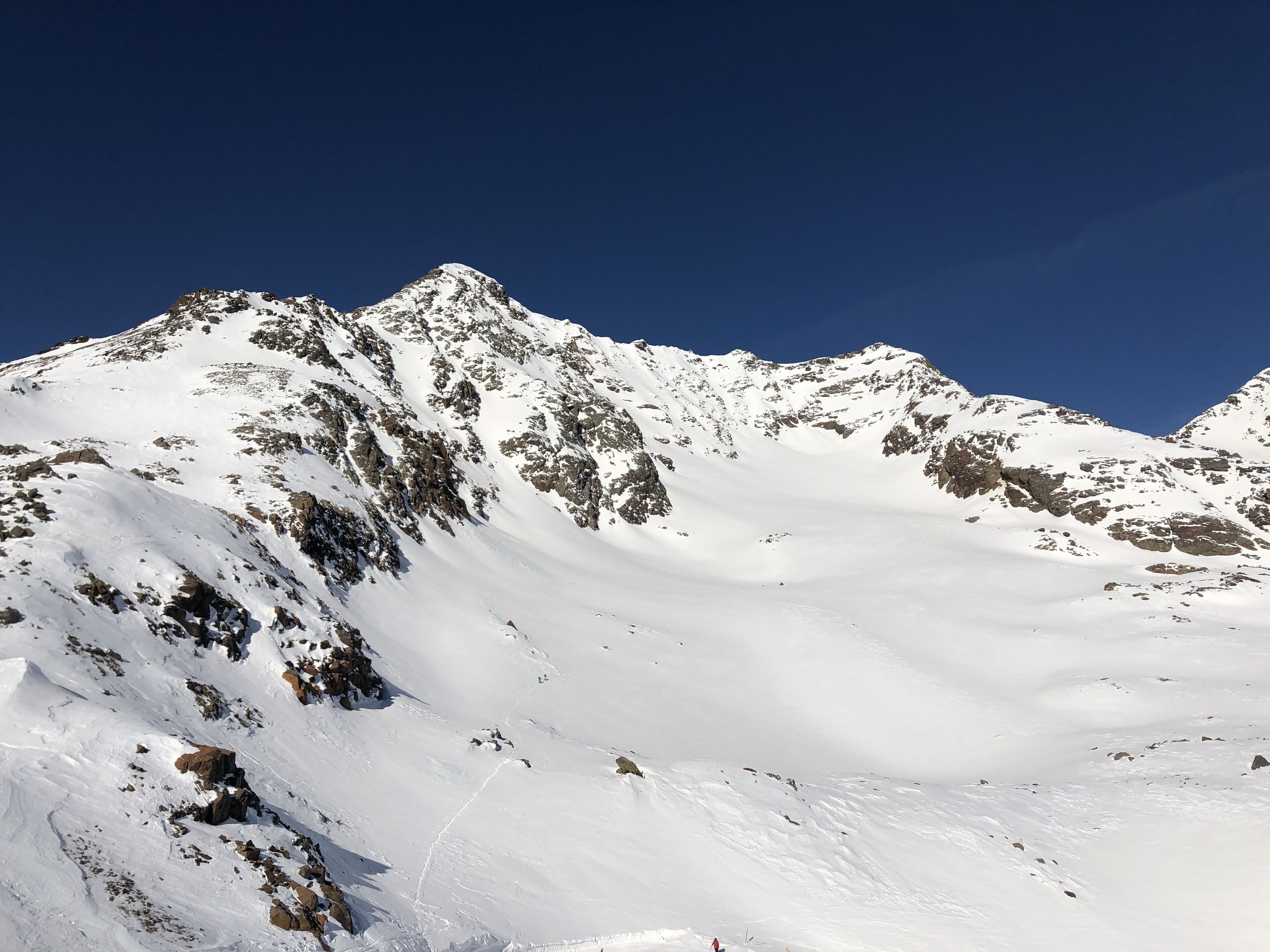 A snow-covered mountain with rocky outcrops and a clear blue sky.