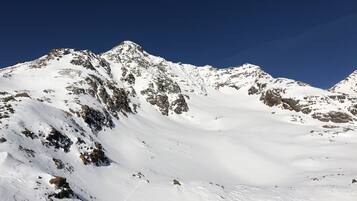 A snow-covered mountain with rocky outcrops and a clear blue sky.