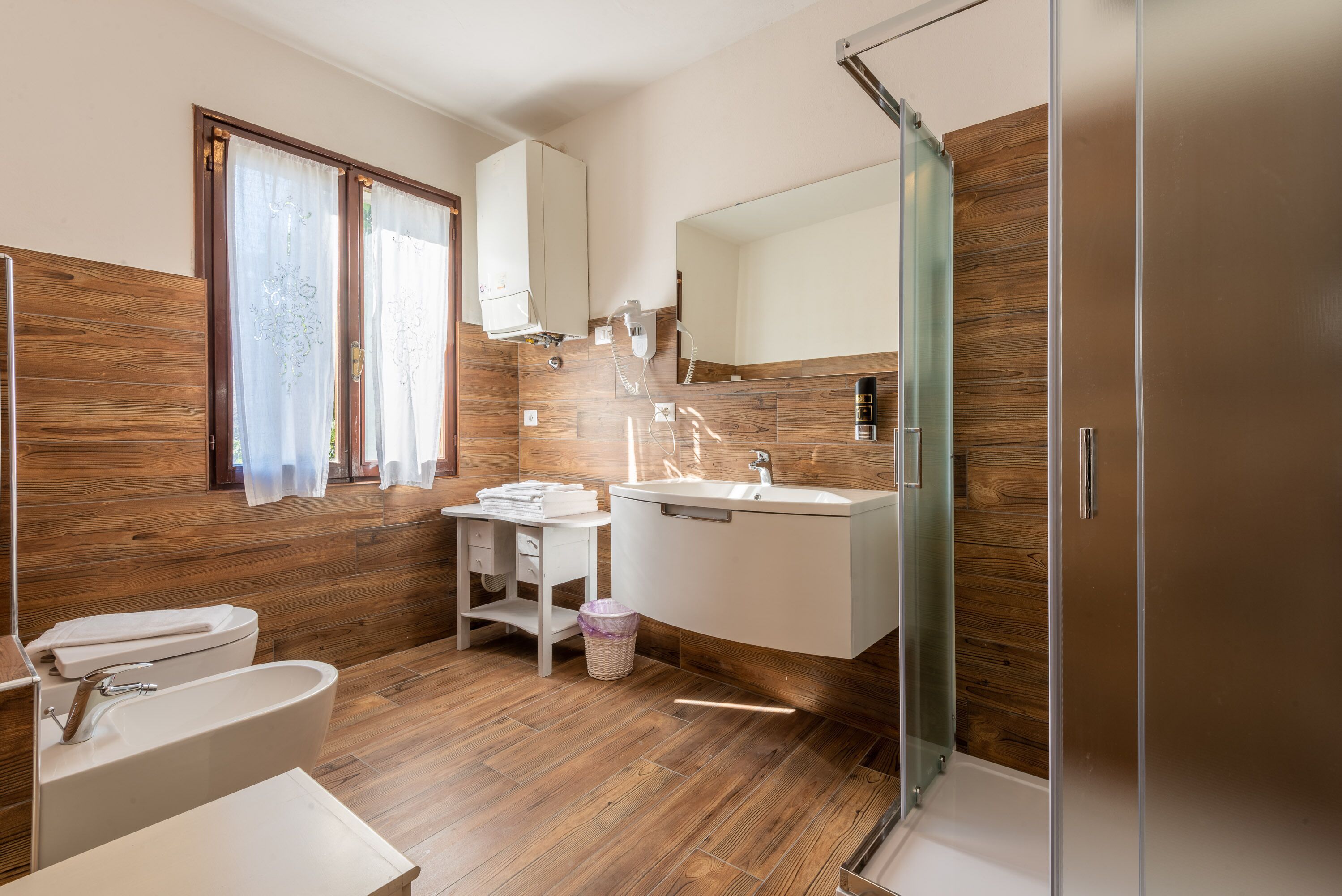 A modern bathroom with wooden flooring, a freestanding bathtub, a vanity with a mirror, and a shower enclosure.