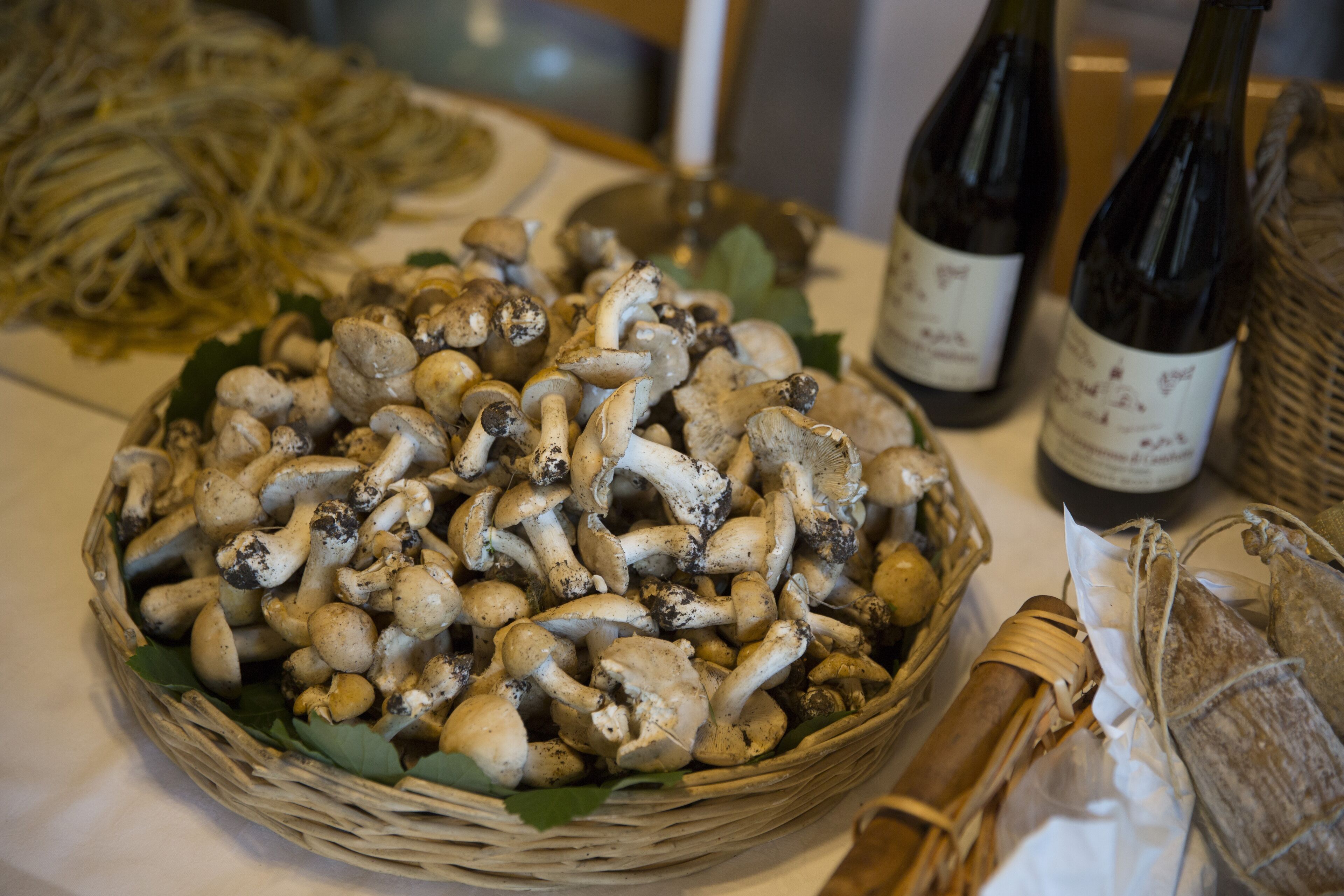 Un panier de champignons est posé sur une table, à côté de deux bouteilles de vin et d’un autre panier en osier.