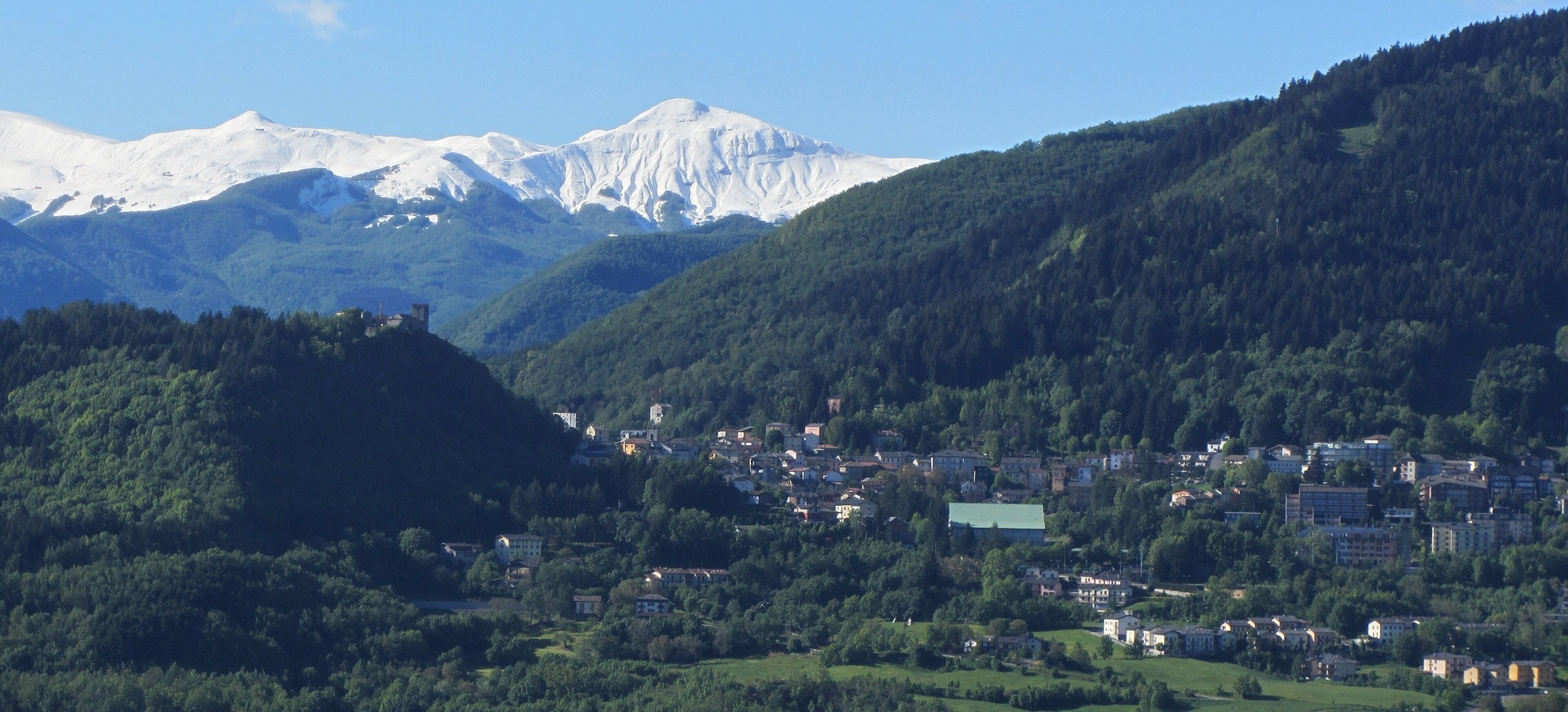 A town nestled in a valley with snow-capped mountains in the background.