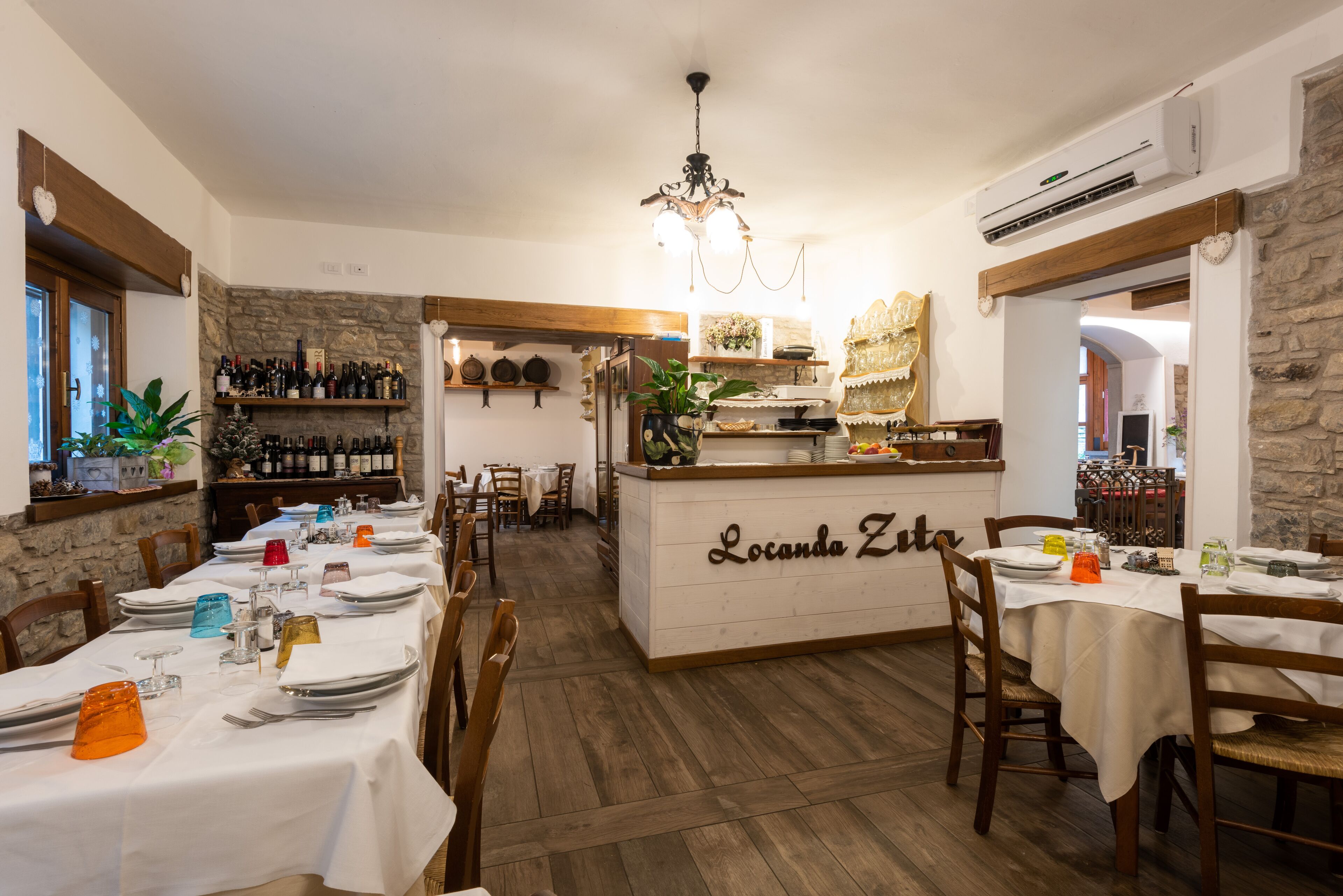 Un restaurante con mesas y sillas de madera, una zona de bar central y una pared de piedra.