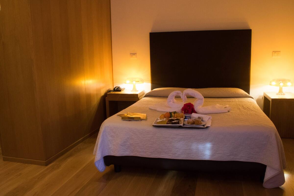A hotel room with a large bed, two bedside tables with lamps, and a wooden floor.