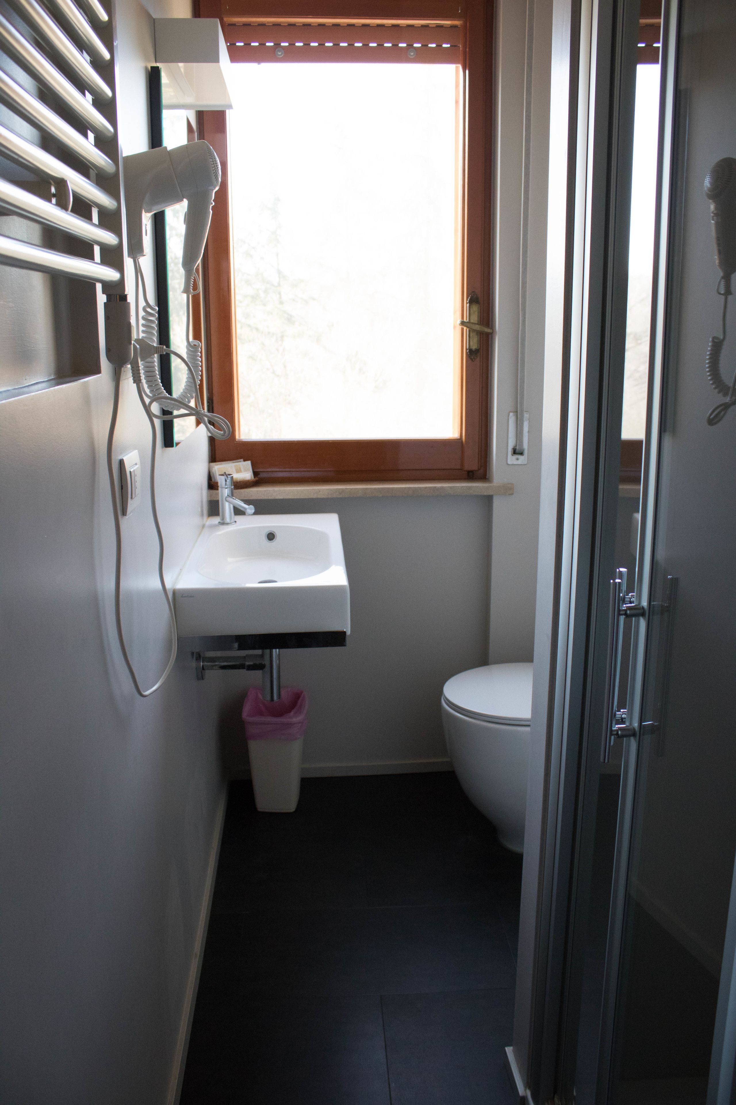 Un baño pequeño con un lavabo blanco, una ventana sobre el inodoro y una zona de ducha.