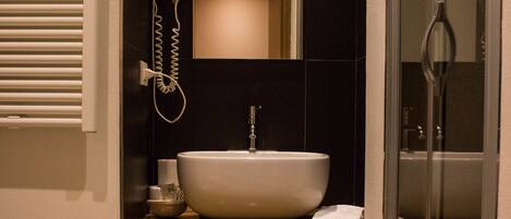 A modern bathroom with a large sink, a hairdryer, a mirror, and a shower enclosure.