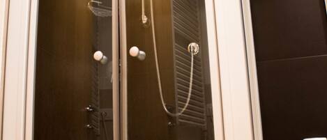A glass-enclosed shower with a handheld showerhead and a wall-mounted faucet.