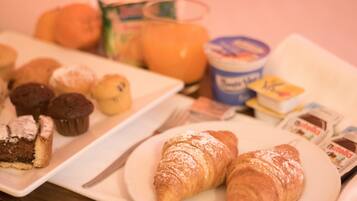A breakfast table with pastries, a plate of muffins, a glass of orange juice, and a container of yogurt.